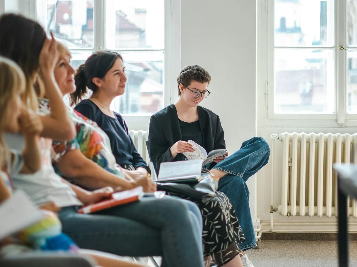 A small group seated in a circle in a bright room with tall windows