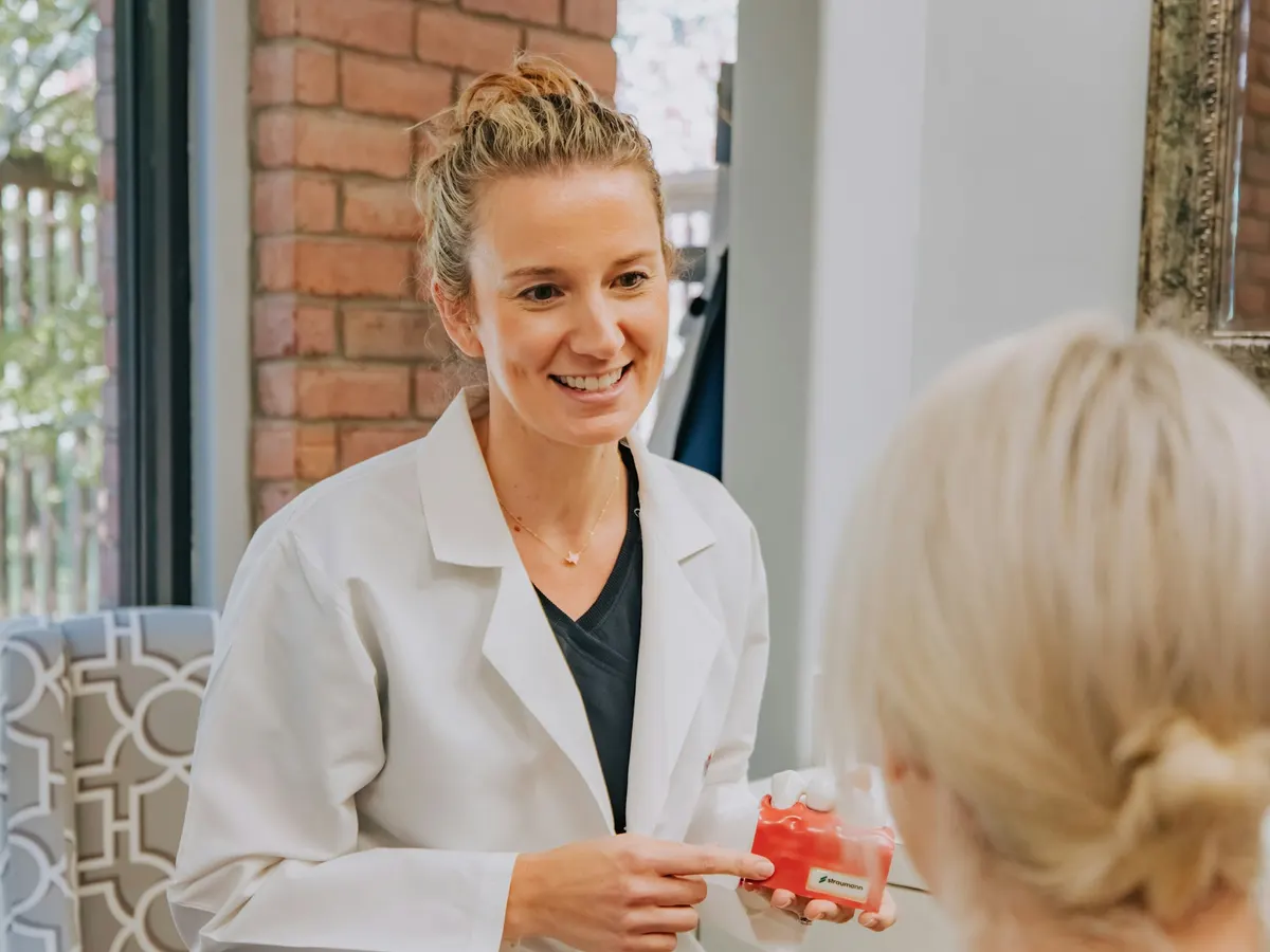 A clinician in a white coat smiling as she talks a patient through a pill organizer